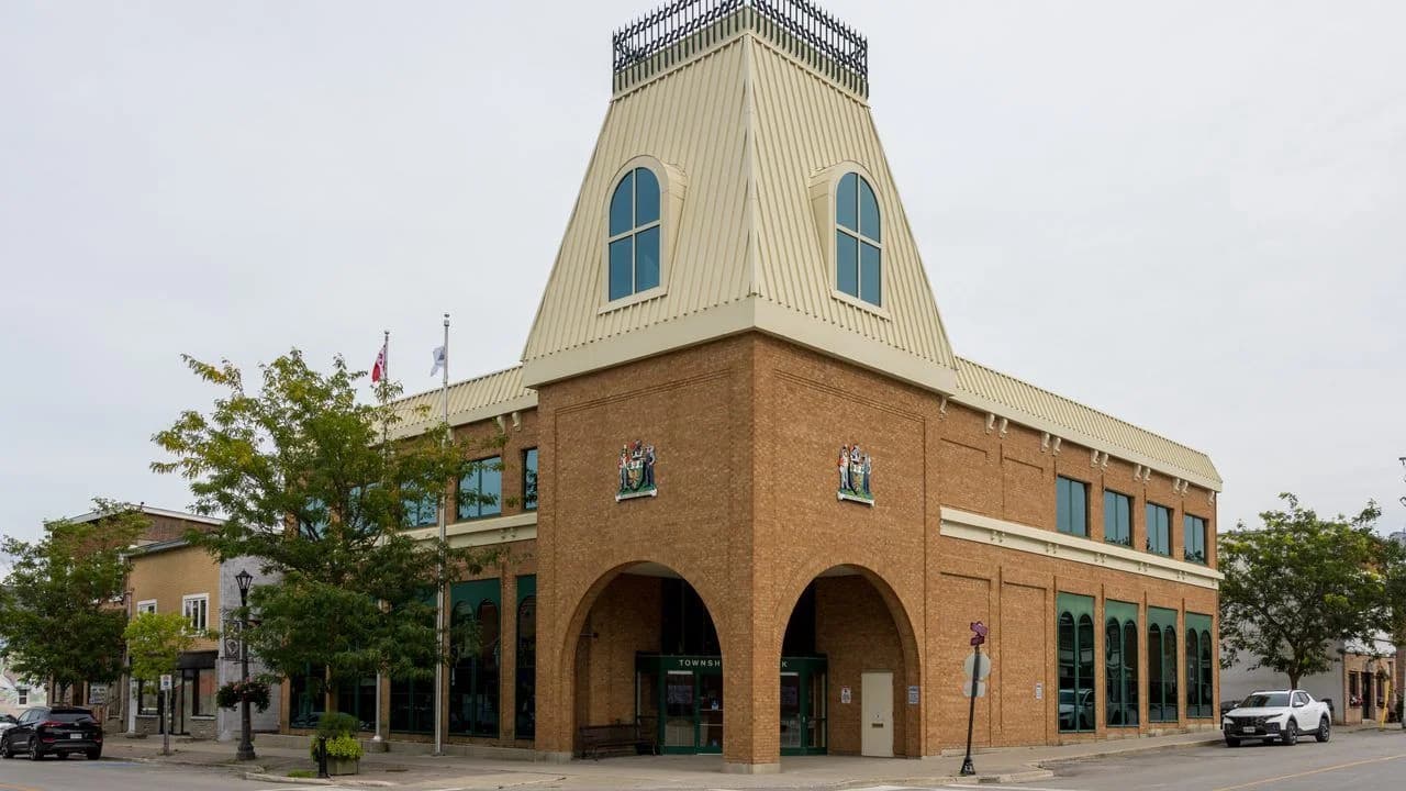 The two-storey brick municipal office building for Brock Township in downtown Cannington, Ontario, with a peaked metal roof, arched entrance and township crests, and no people visible