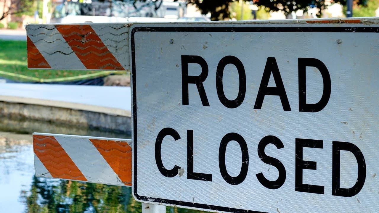 A "Road Closed" sign on orange-and-white striped barricades; no people visible