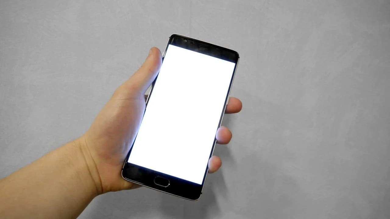 A hand holding a smartphone with a blank white screen, evoking online device use by youth