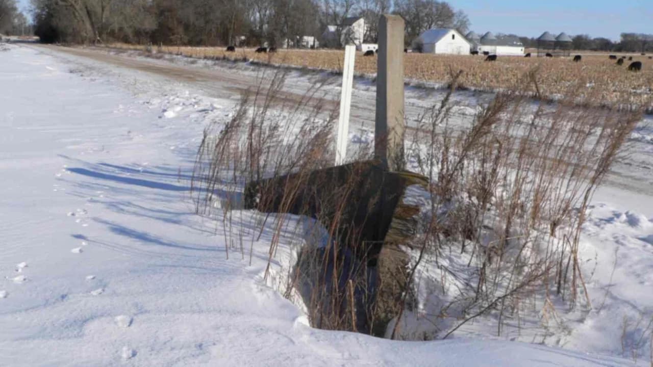 Concrete culvert marker post beside a snow-covered rural road