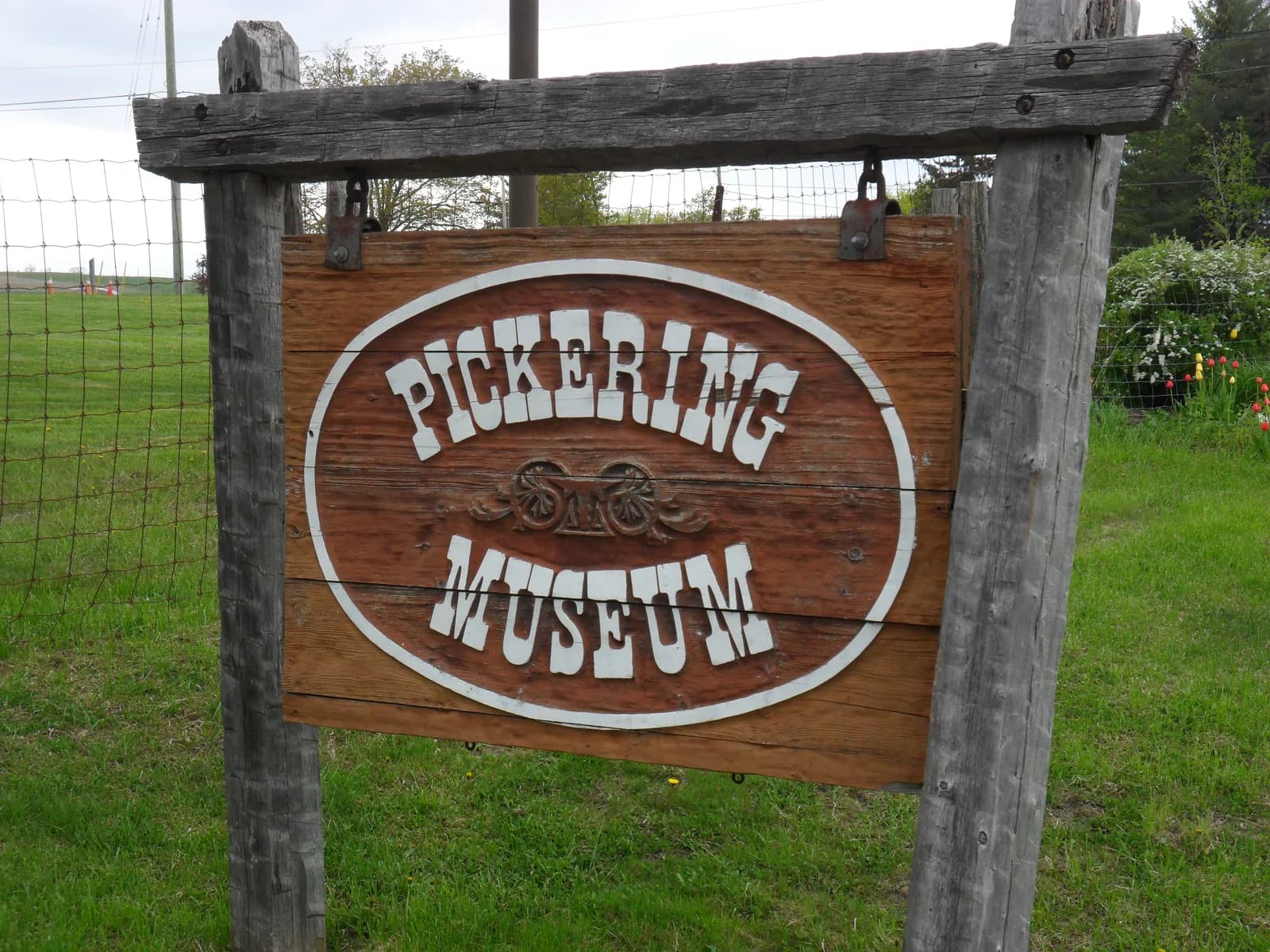 Wooden Pickering Museum sign beside grass and spring flowers.