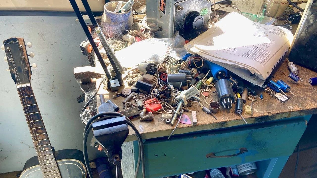 Electronics repair workbench with tools, test equipment, cables and components; no people visible.