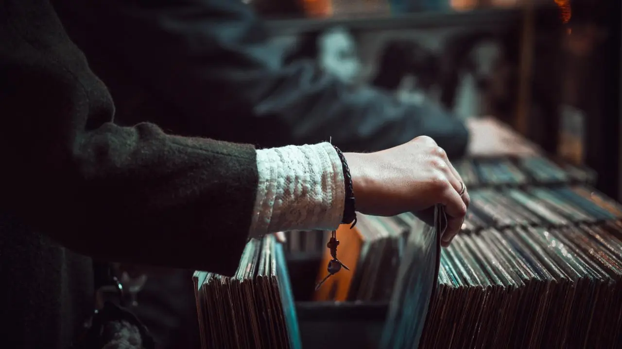 A hand browsing vinyl records in bins at a record store; no faces visible.